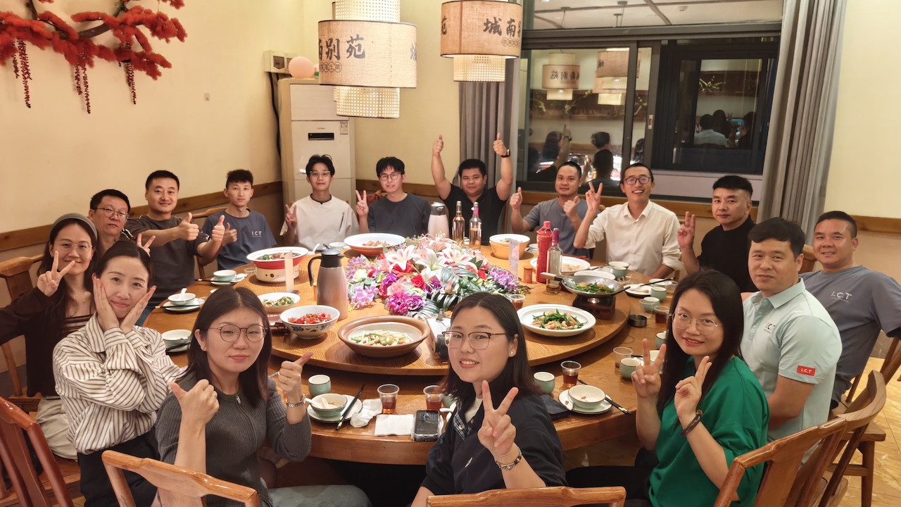 A group photo of I.C.T team members enjoying a celebratory dinner, with smiles and peace signs, marking the addition of four new partners to the company.